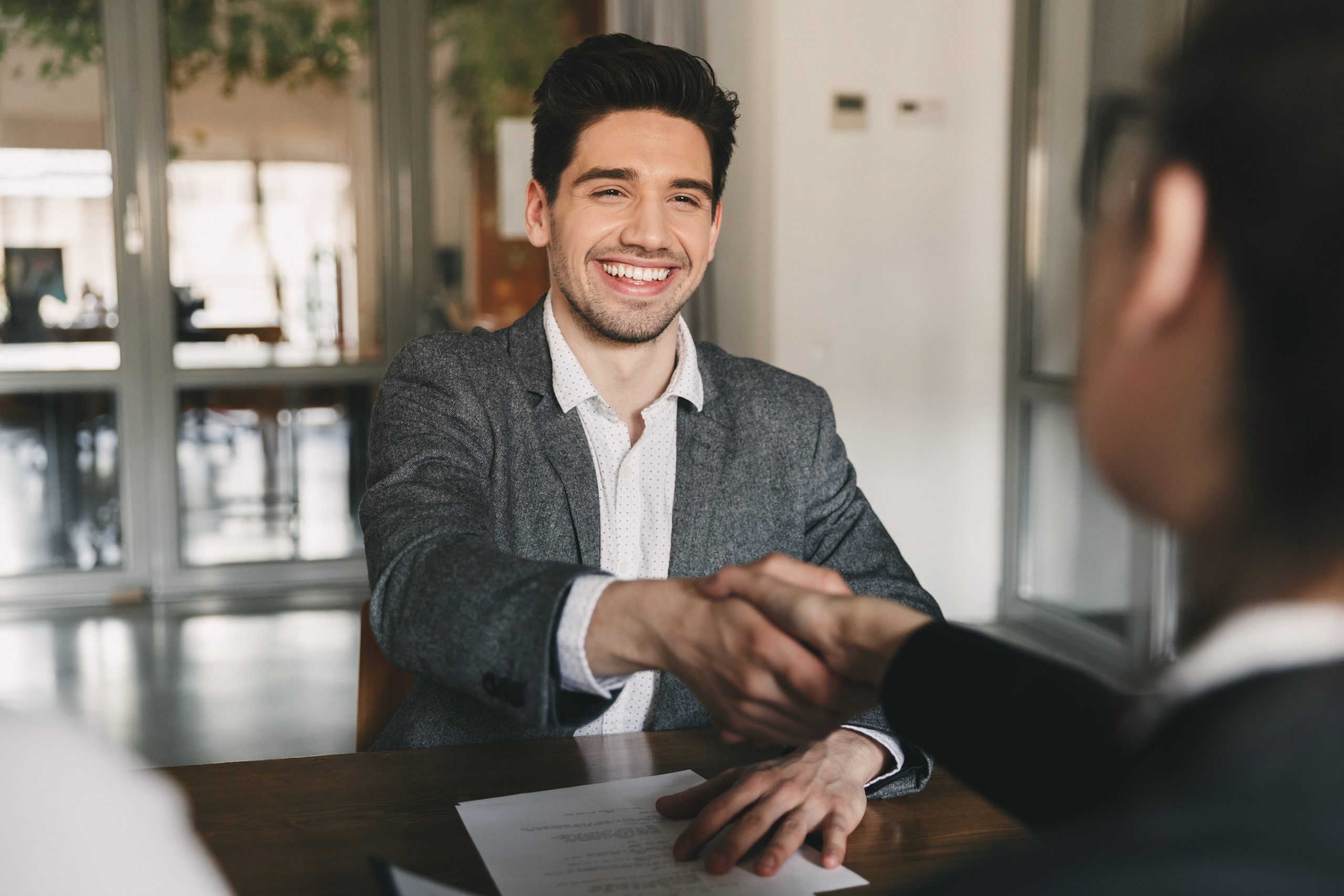 a smiling man and a woman shaking hands during an interview discussing the hiring process. An interview can lead to a job and internship.